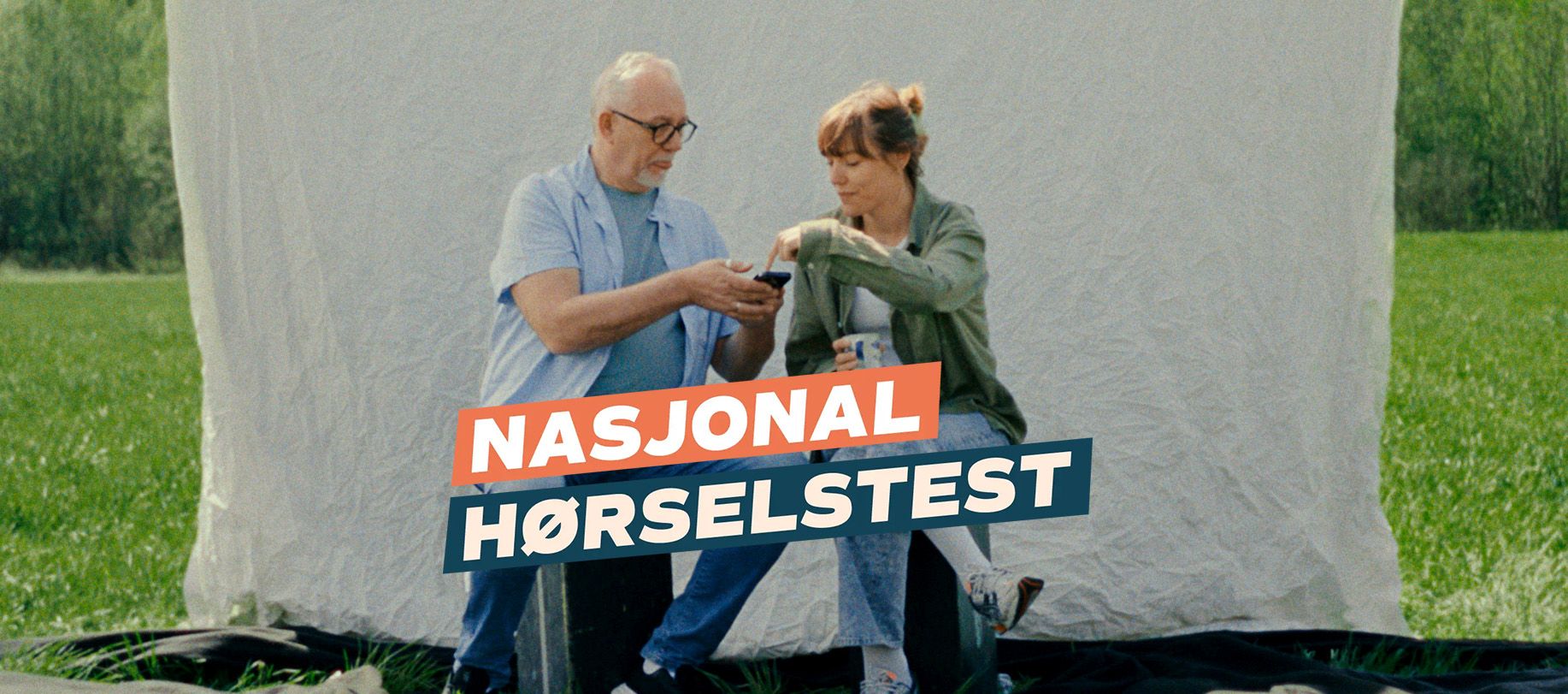 Far og datter sitter foran hvit kulisse og trykker på en mobiltelefon