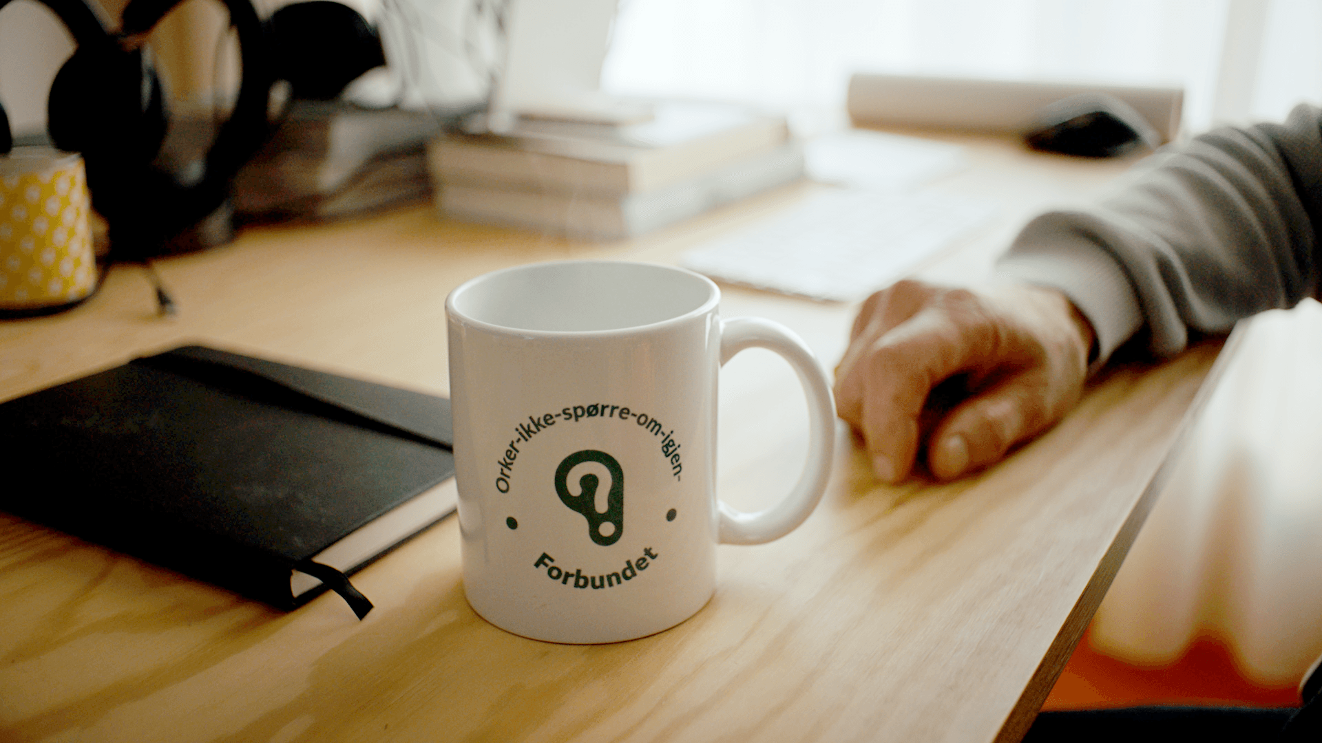 Nærbilde av kontorpult med kaffekopp, med logoen Orker-ikke-spørre-om-igjen-forbundet.